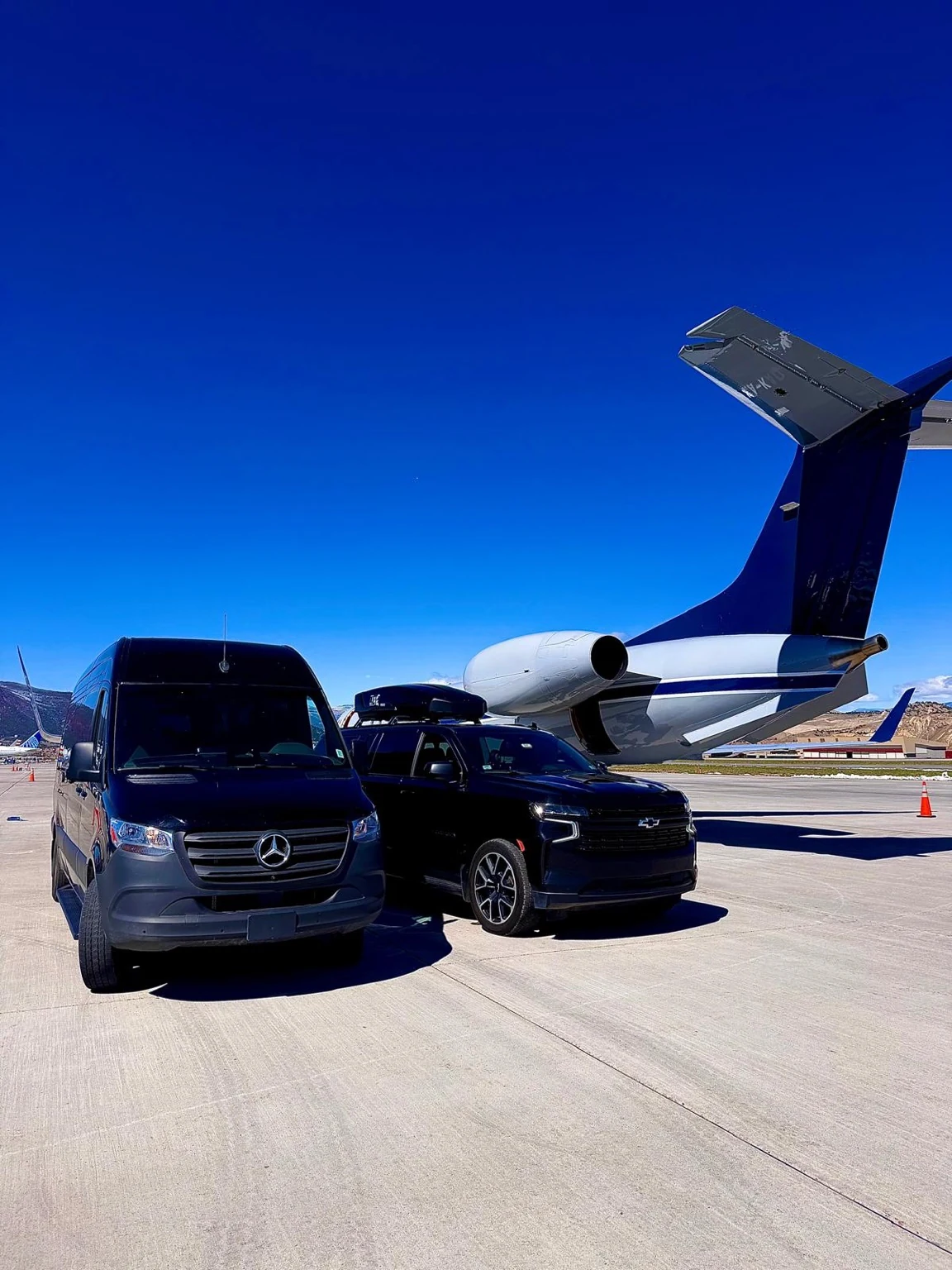 Elite Ride passenger van and Chevrolet Suburban beside a private aircraft